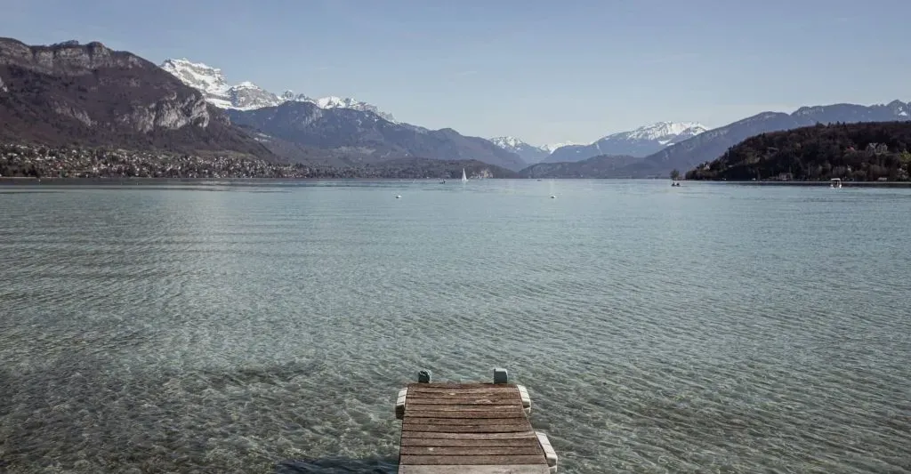 Ponton bois sur lac d'Annecy avec montagnes enneigées au loin.